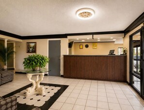 A reception area with a reception desk, a clock, and a potted plant. - Rodeway Inn Expo Center (Spartanburg)