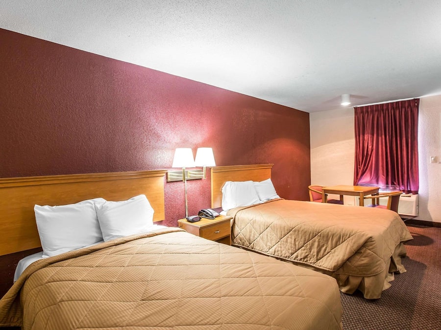 A hotel room with two beds, a desk, a chair, and a window with curtains.