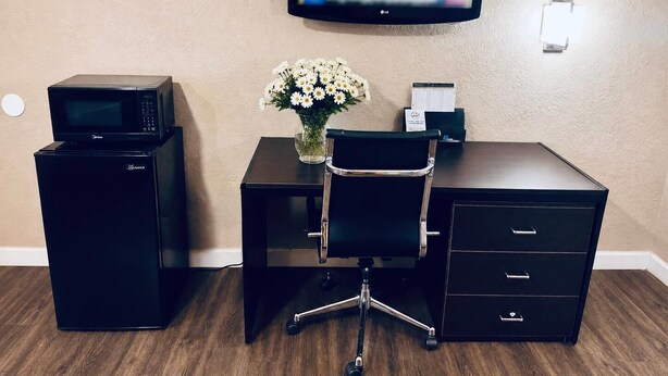Habitación de hotel con escritorio, microondas, televisor, florero con flores y archivador.