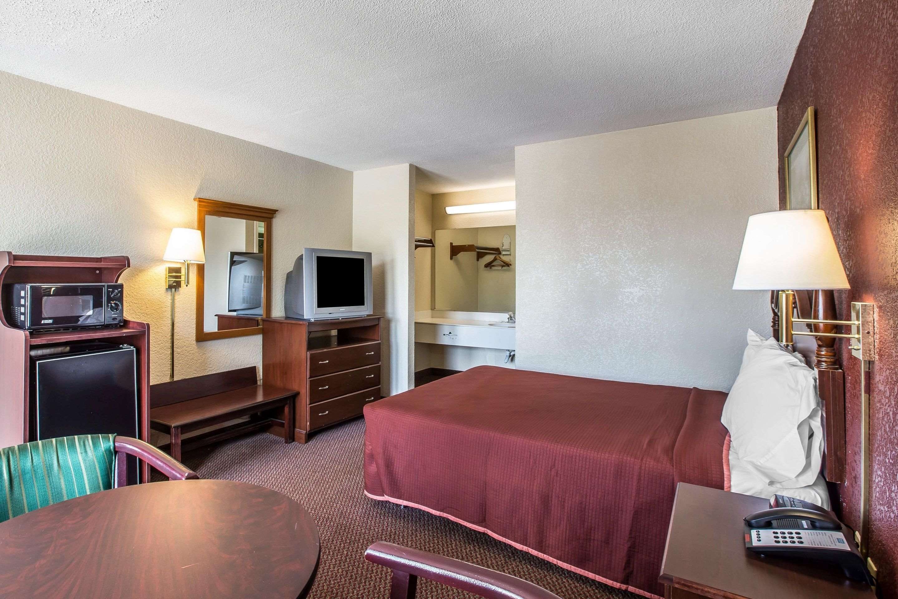 Habitación de hotel con cama, escritorio con teléfono, televisor, microondas, refrigerador pequeño y espejo.