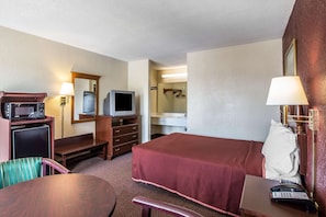 A hotel room with a bed, a desk with a telephone, a television, a microwave, a small refrigerator, and a mirror. - Rodeway Inn Expo Center (Spartanburg)