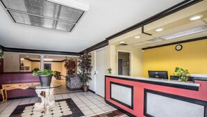 Zona de recepción con mostrador de entrada, escritorio, planta en maceta, reloj y suelo de baldosas.