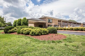 A multi-story hotel with a brick facade, a covered entrance, and a landscaped front yard with hedges and mulch.