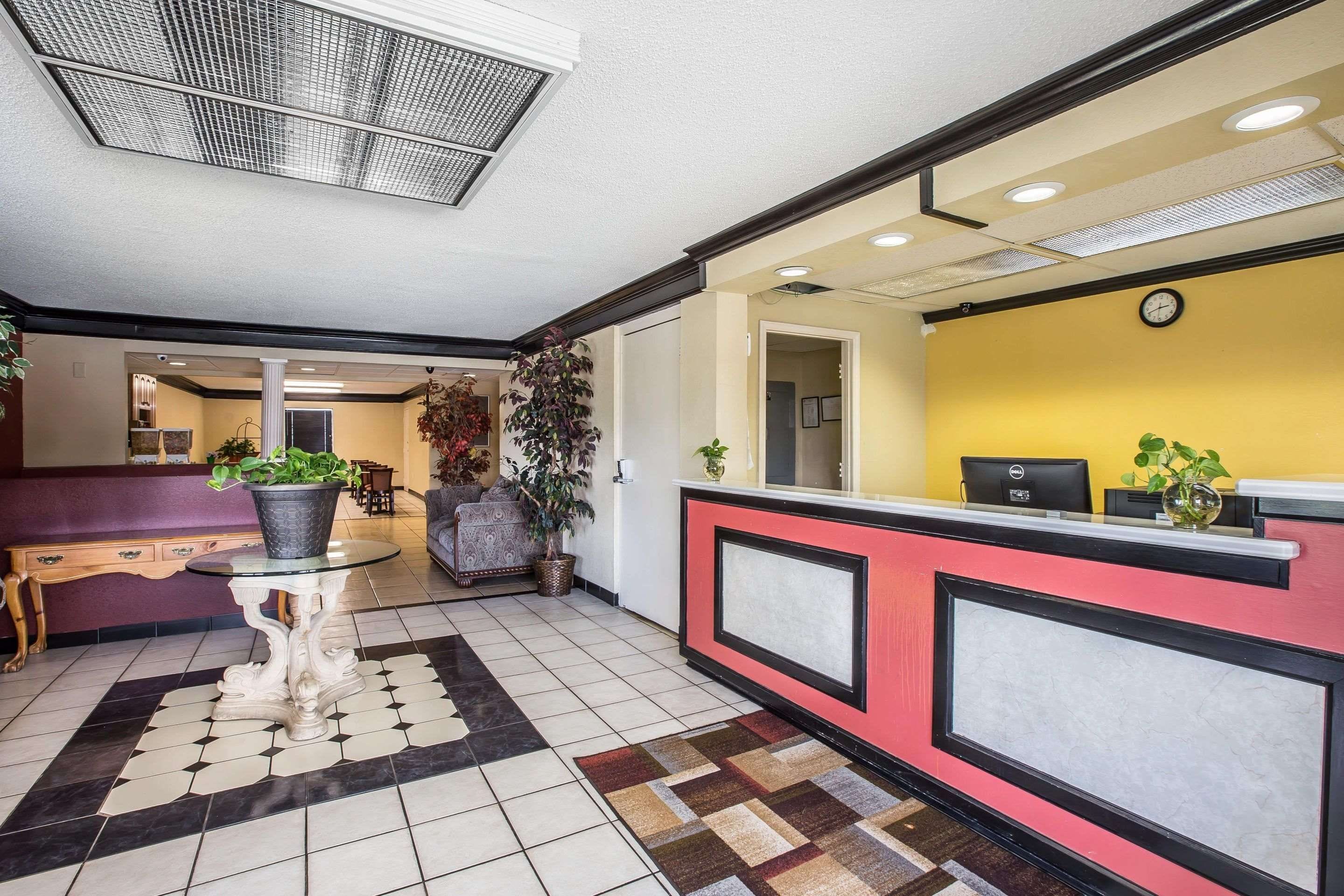 A hotel reception area with a check-in counter, a seating area with a table and chairs, and a hallway leading to other rooms.