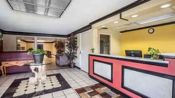 A hotel reception area with a check-in counter, a seating area with a table and chairs, and a hallway leading to other rooms.