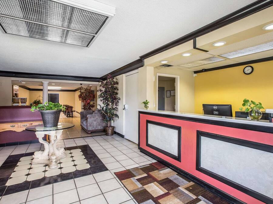A hotel reception area with a check-in counter, a seating area with a table and chairs, and a hallway leading to other rooms.