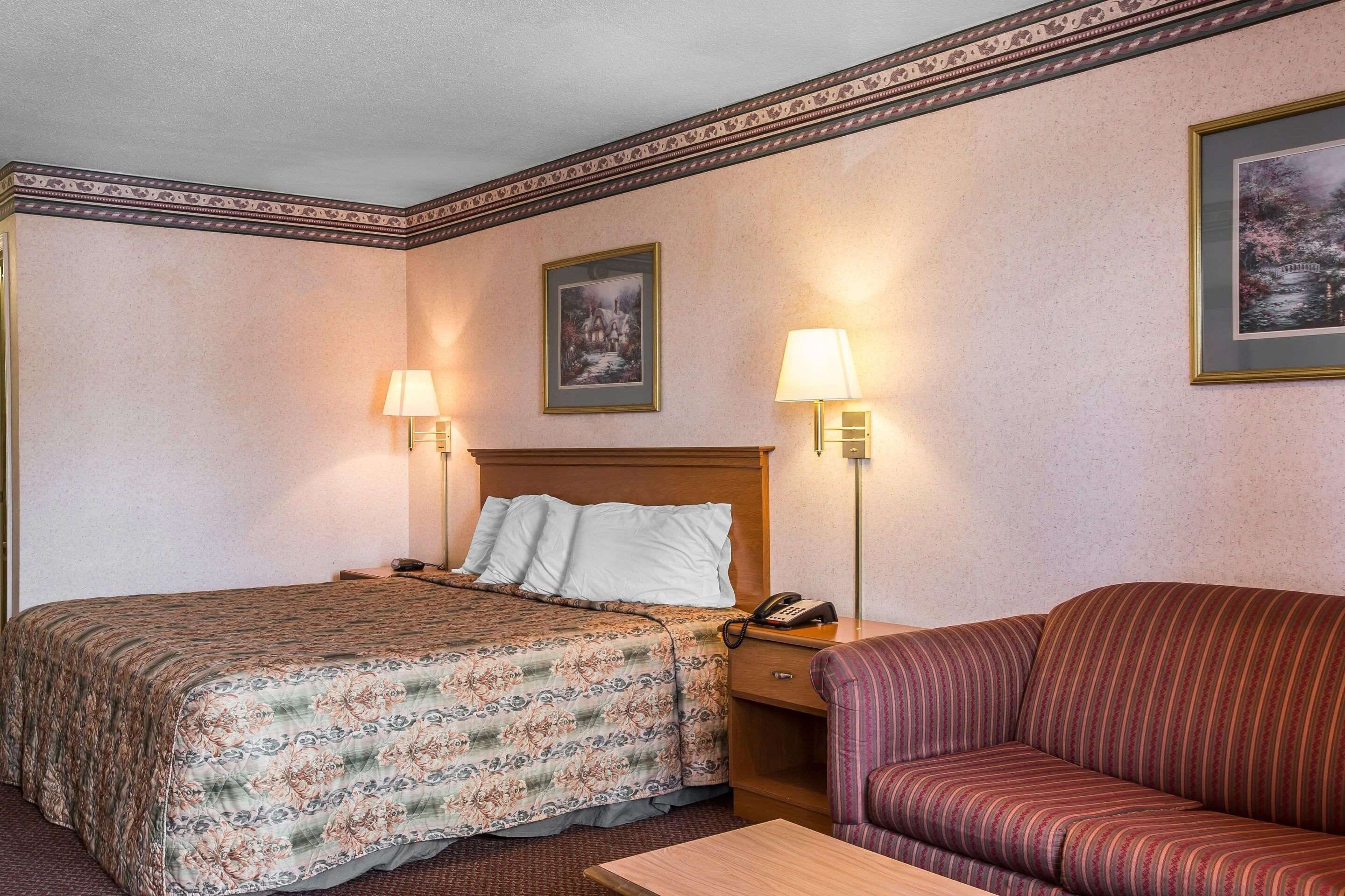 A hotel room with a bed, a sofa, two wall-mounted lamps, a nightstand with a phone, and two framed pictures on the wall.