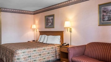 A hotel room with a bed, a sofa, two wall-mounted lamps, a nightstand with a phone, and two framed pictures on the wall.