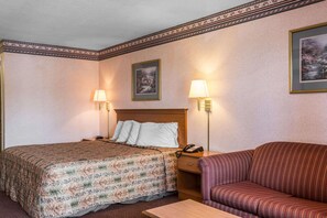 A hotel room with a bed, a sofa, two wall-mounted lamps, a nightstand with a phone, and two framed pictures on the wall.