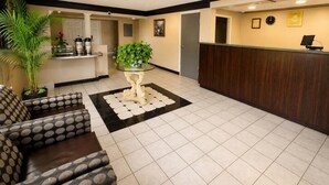 Una hall d'albergo con una reception, una macchina per caffè, una pianta in vaso, un divano e un pavimento piastrellato.