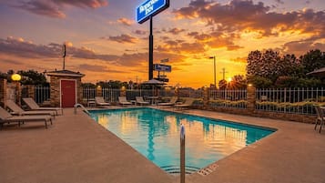 Zona de piscina con sillones de descanso, un cartel de Rodeway Inn y un atardecer de fondo.
