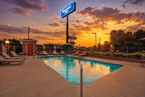 A pool area with lounge chairs, a sign for Rodeway Inn, and a sunset in the background.