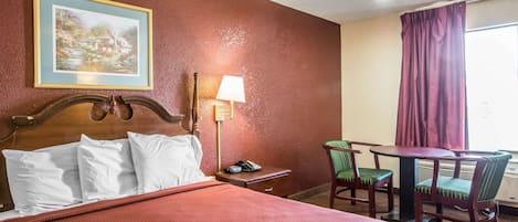 Una habitación de hotel con cama, escritorio con lámpara, silla y mesa.
