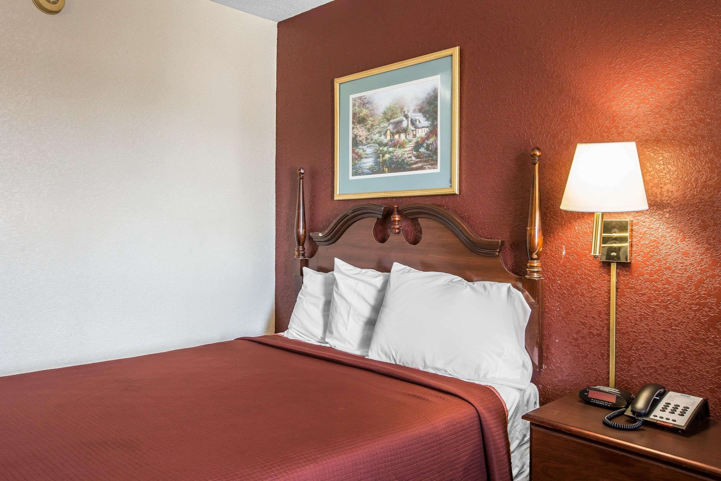 A hotel room with a bed, a bedside lamp, a telephone, and a framed picture on the wall.