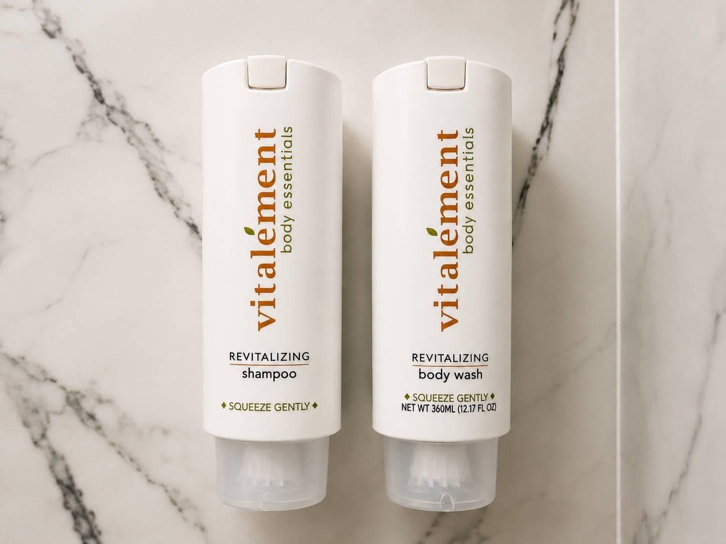 Two bottles of Vitalement body essentials, one shampoo and one body wash, with a marble background.