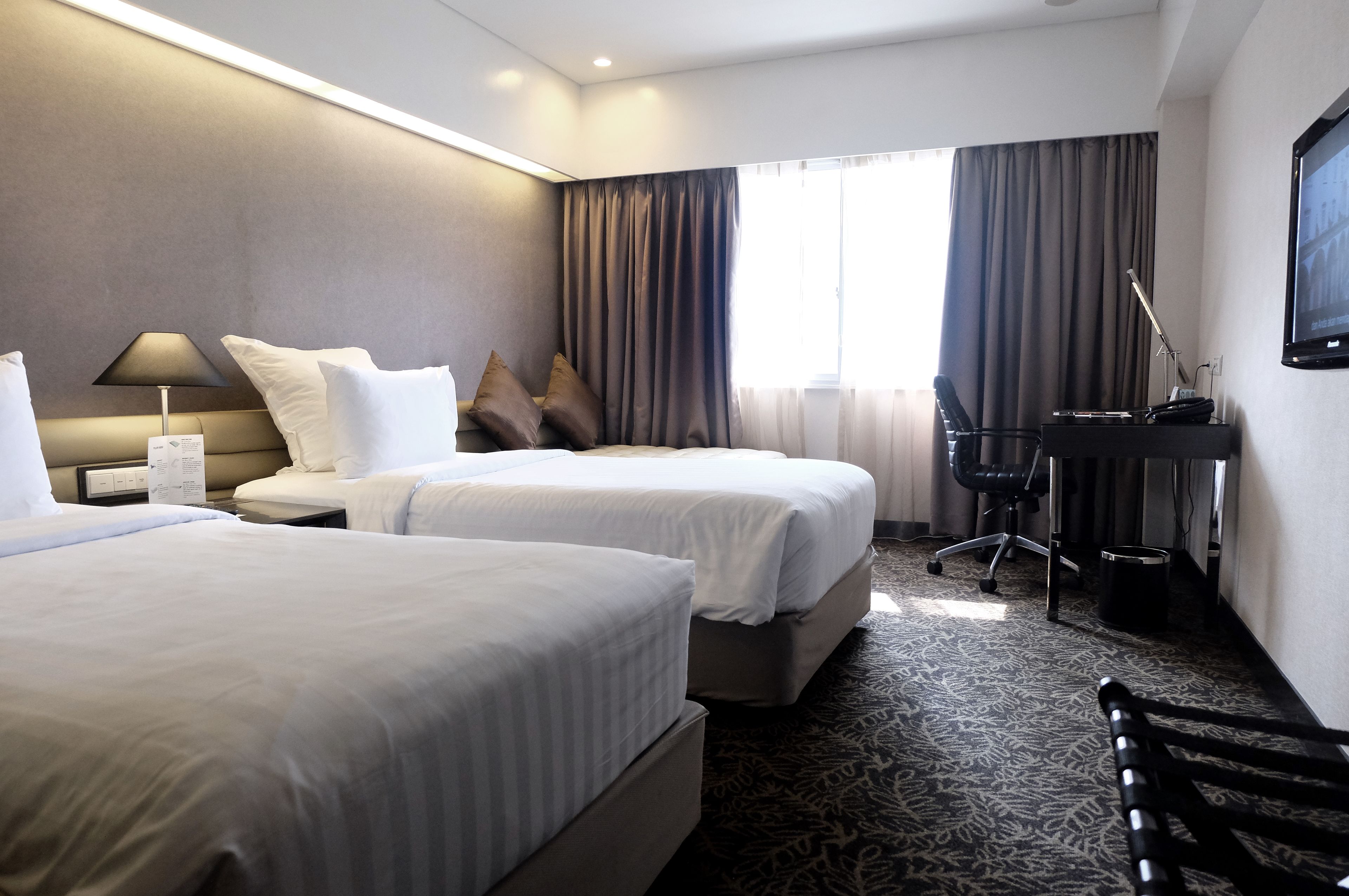 A hotel room with two beds, a desk, a chair, and a TV.