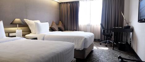 A hotel room with two beds, a desk, a chair, and a TV.