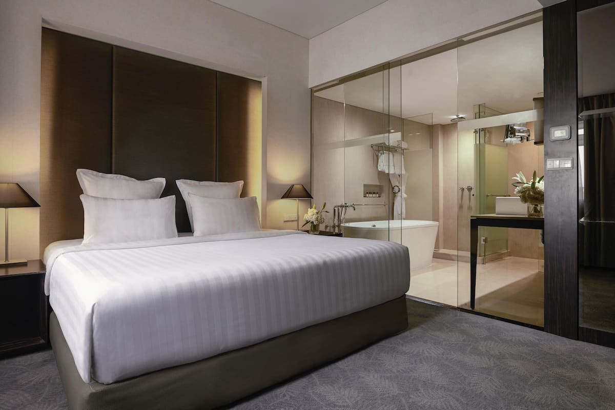 A modern hotel room with a large bed, a glass-enclosed bathroom, and a separate shower area.