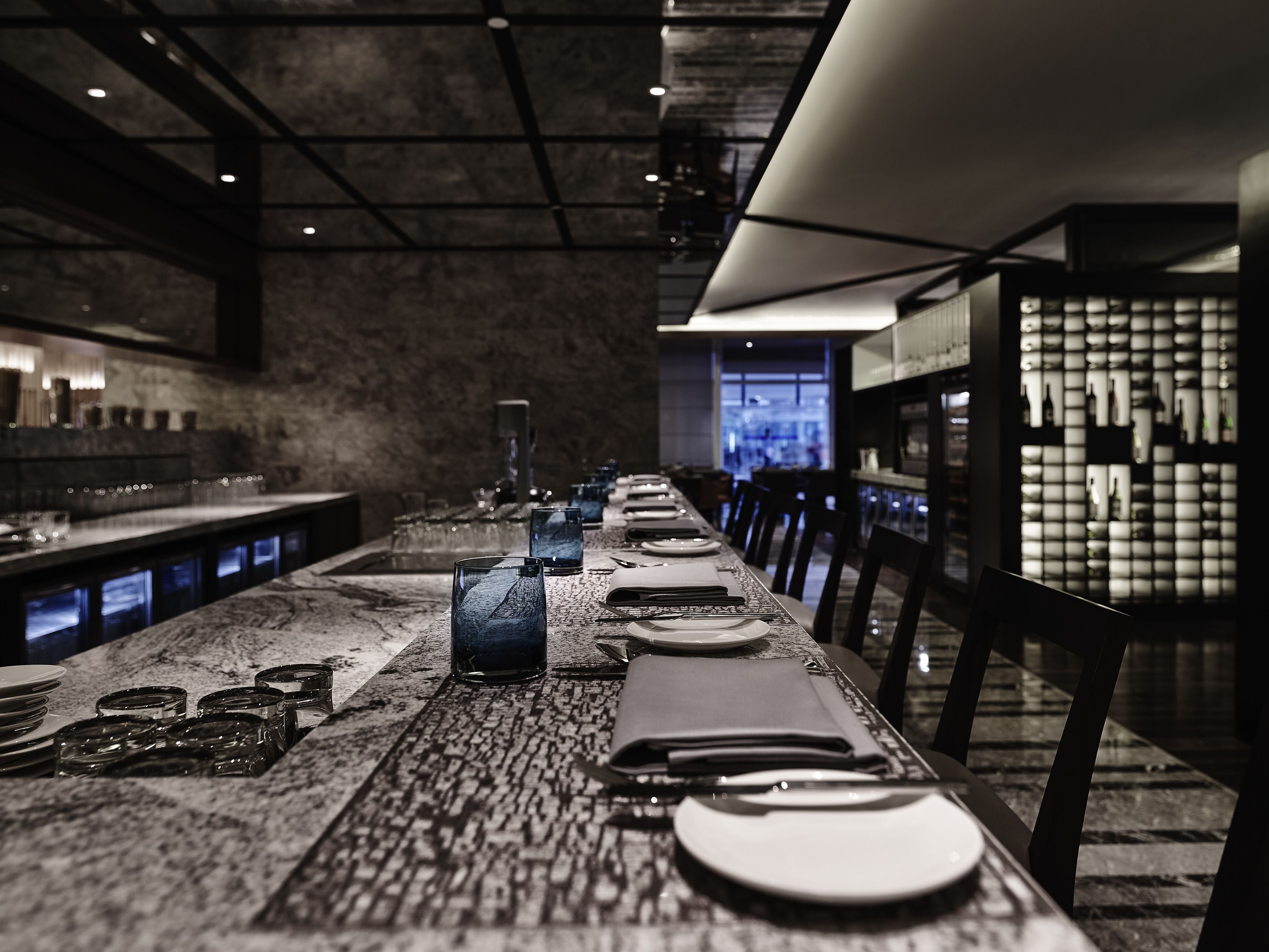 A long dining table set with plates, glasses, and cutlery, with chairs on either side.