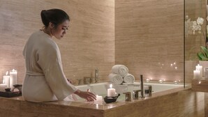 A person in a robe at a bathroom counter with candles, a bathtub, and towels. - Pullman Jakarta Indonesia (Jakarta)