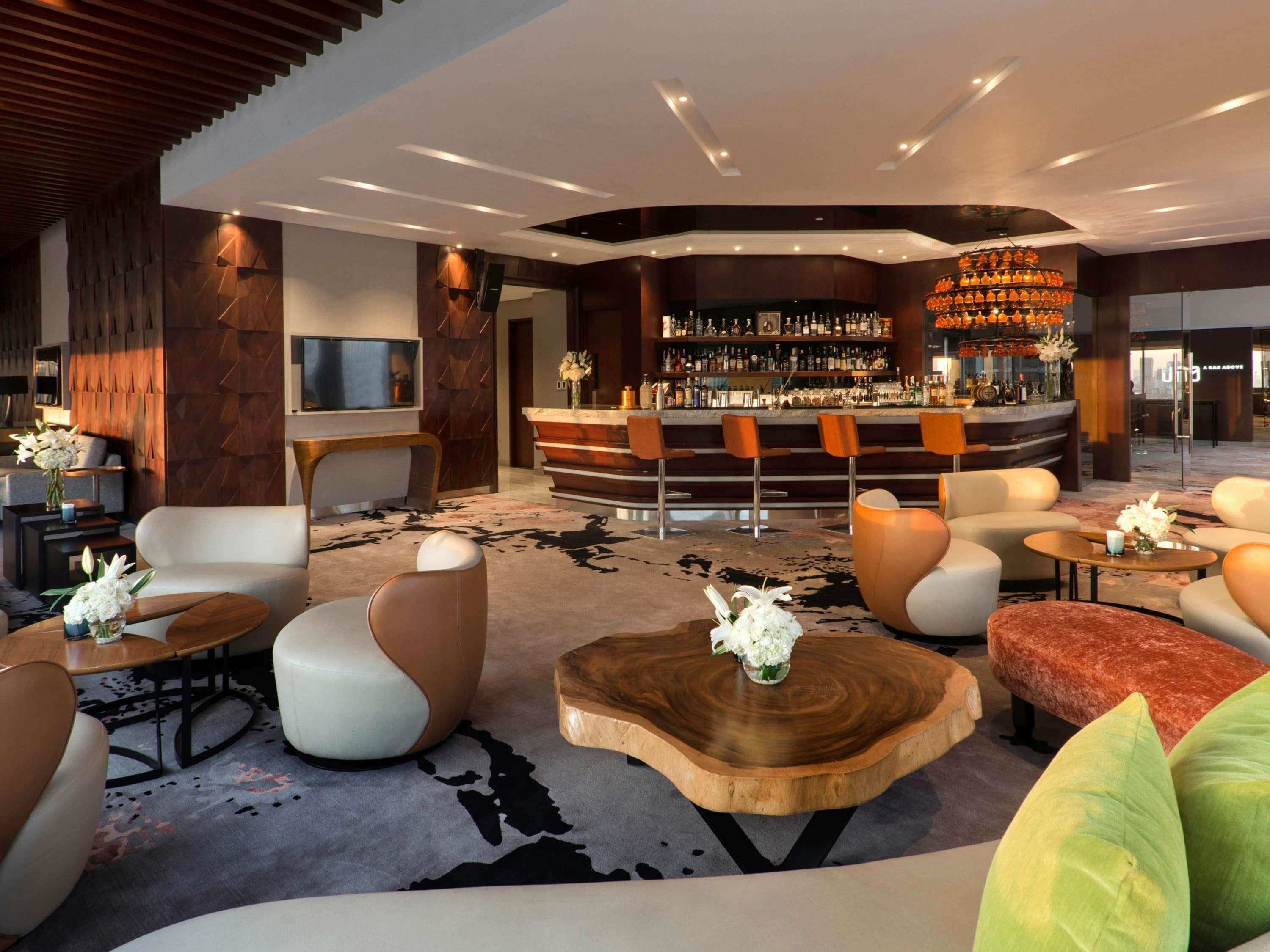 A modern lobby with a bar area, seating arrangements, and a large wooden coffee table.