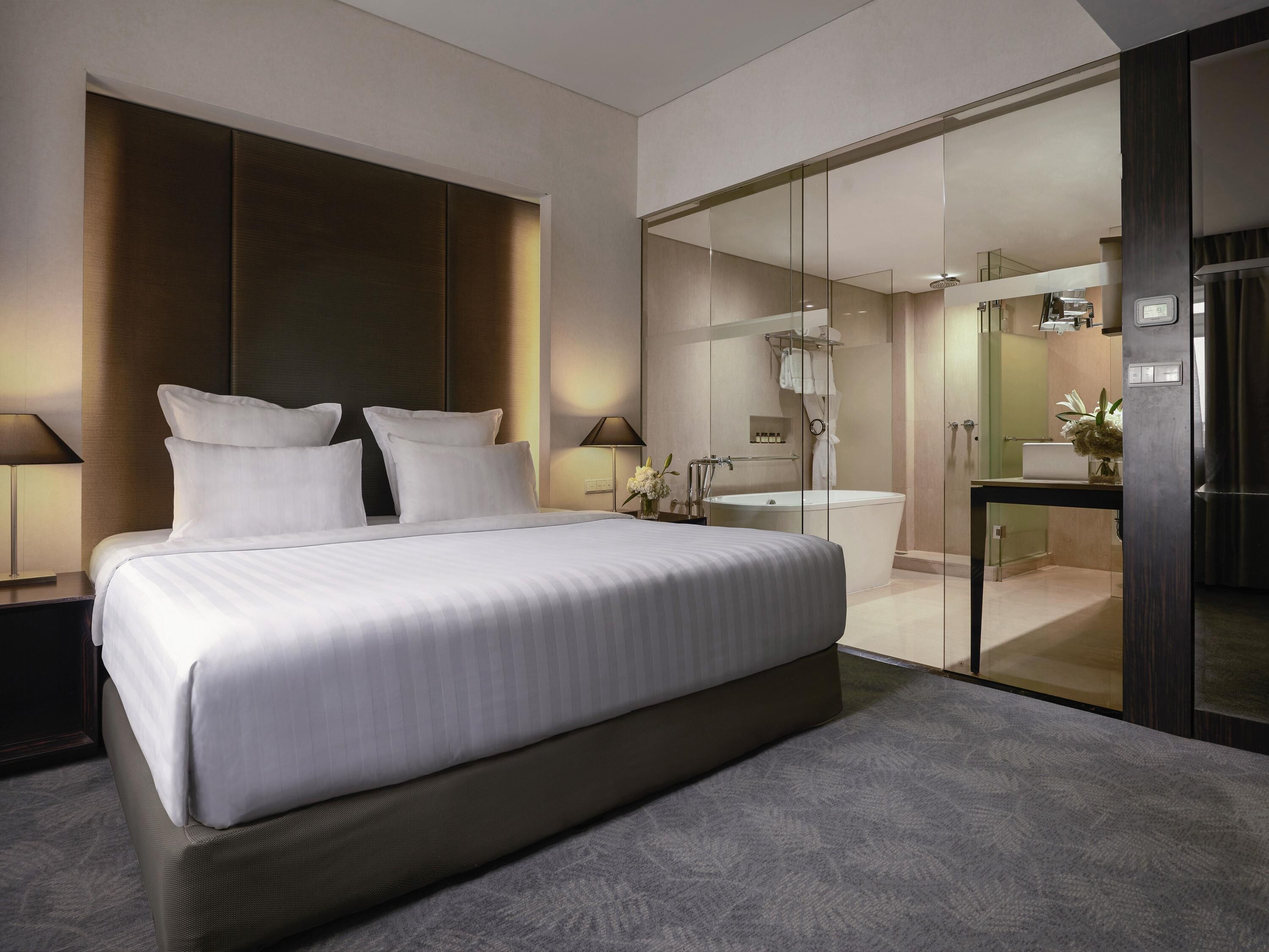 A modern hotel room with a large bed, a glass-enclosed bathroom, and a separate shower area.