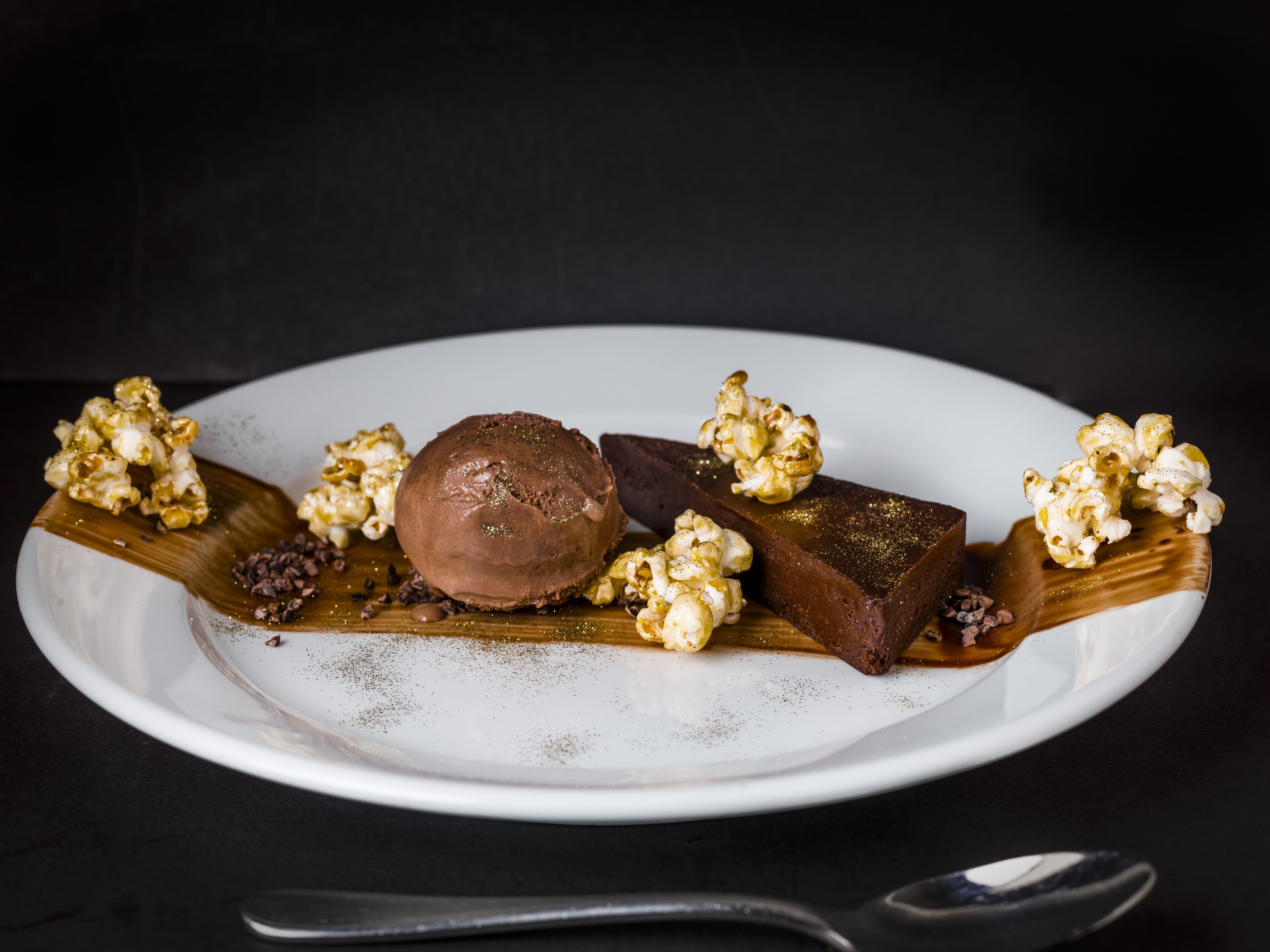 A dessert plate with chocolate ice cream, caramel popcorn, and a chocolate bar.