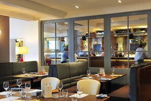 A restaurant with booths and tables, a bar area, and a view of the kitchen. - White Lion Hotel - Aldeburgh (Aldeburgh)