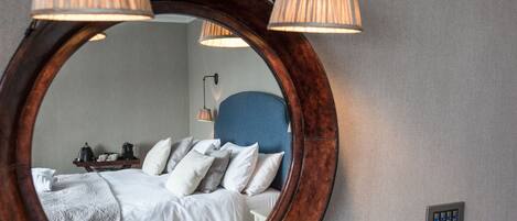 A bedroom with a large mirror, a bed with white linens, and two bedside lamps.