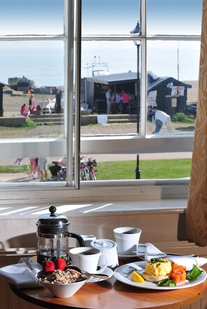 A breakfast table with a coffee pot, a plate of food, and a view of a beach and people in the background. - White Lion Hotel - Aldeburgh (Aldeburgh)