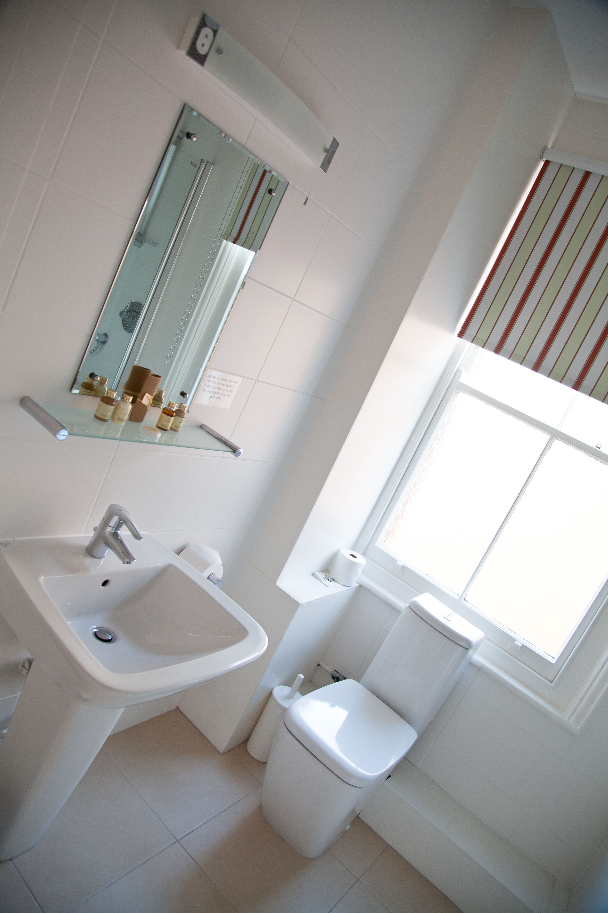 Un baño con lavamanos, espejo, inodoro y ventana con cortinas a rayas.
