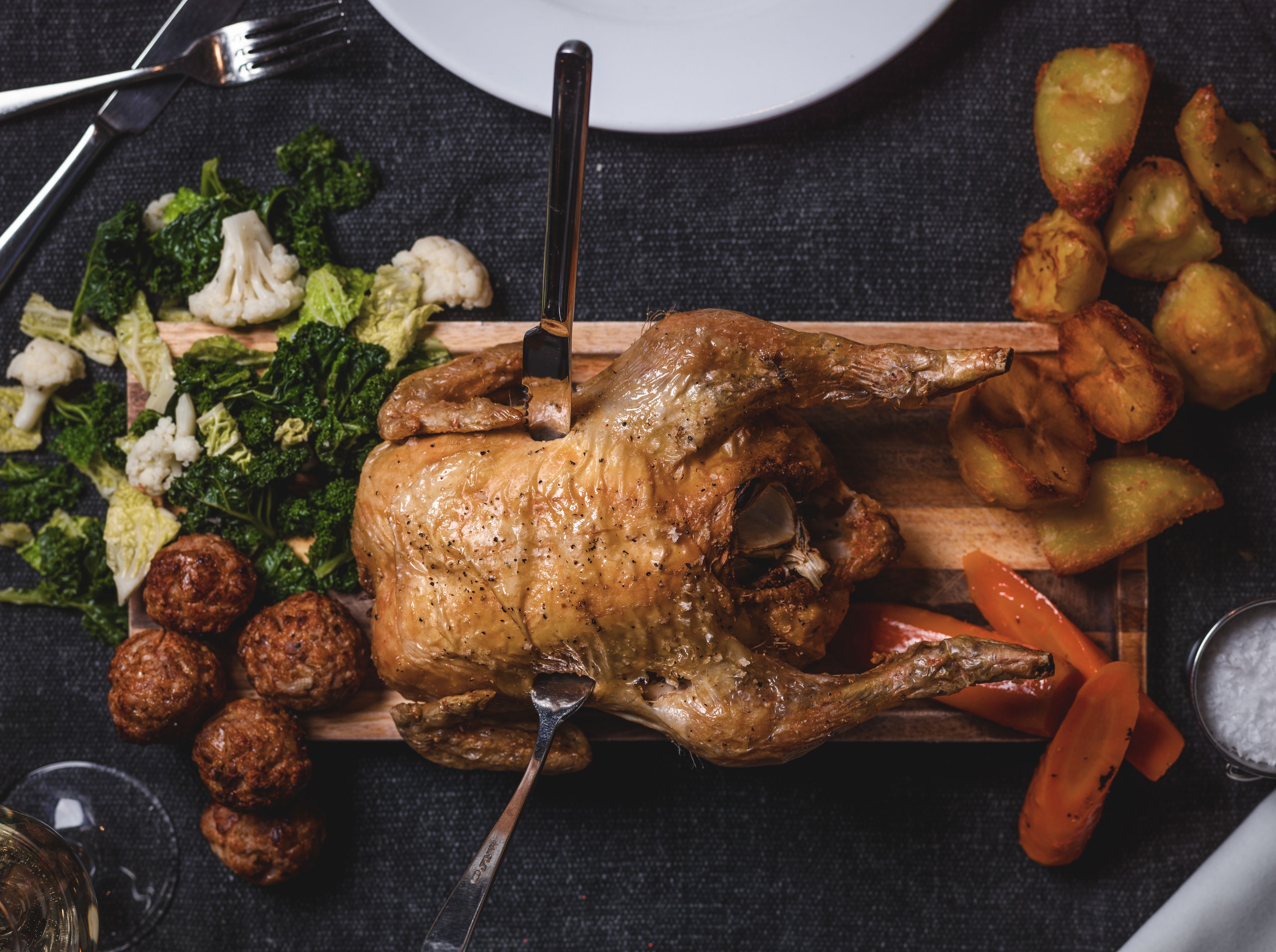 Un poulet rôti, servi sur une planche en bois, accompagné de légumes et de pommes de terre.