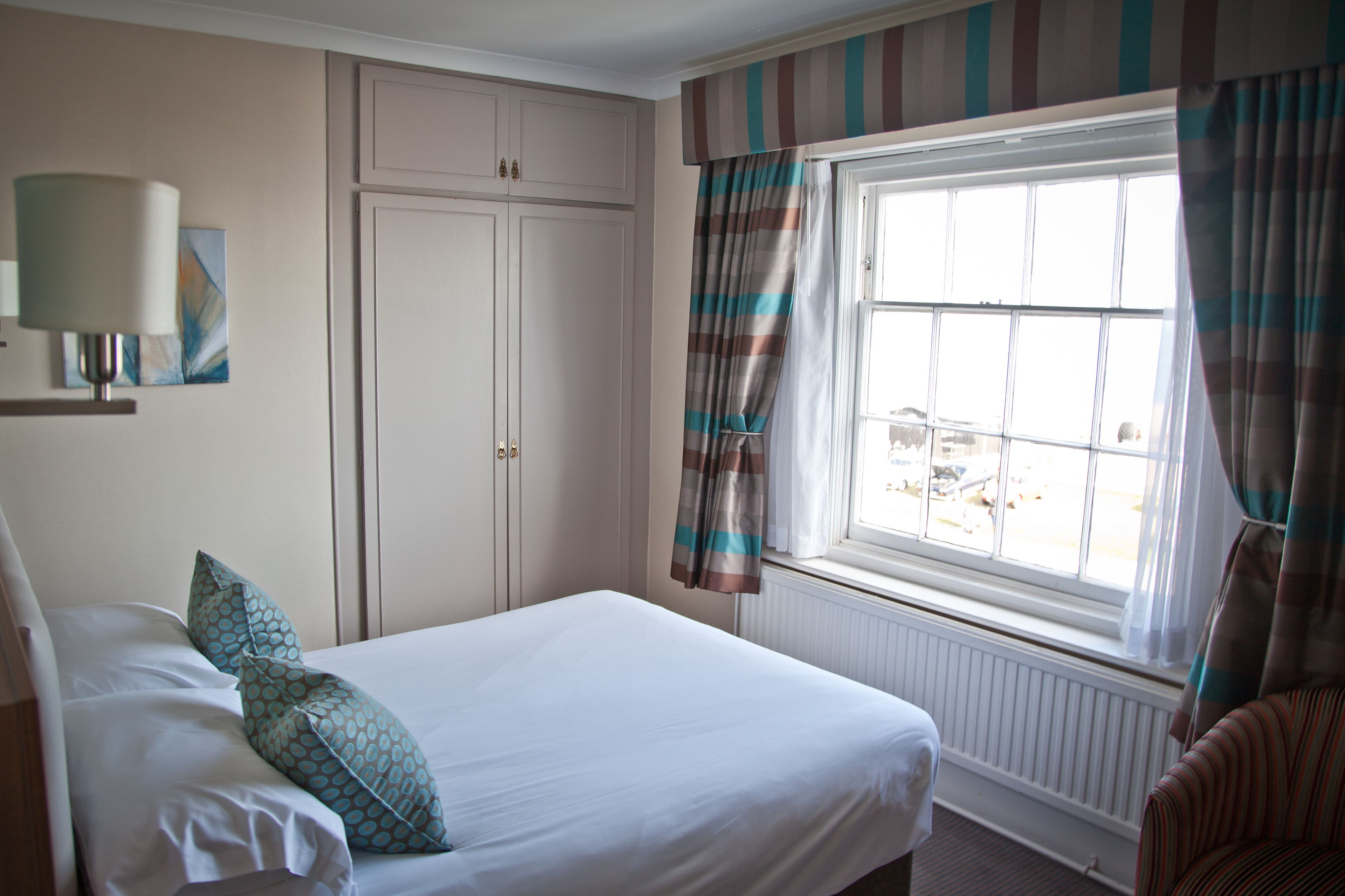 A hotel room with a bed, a window with curtains, a radiator, and a wall-mounted lamp.