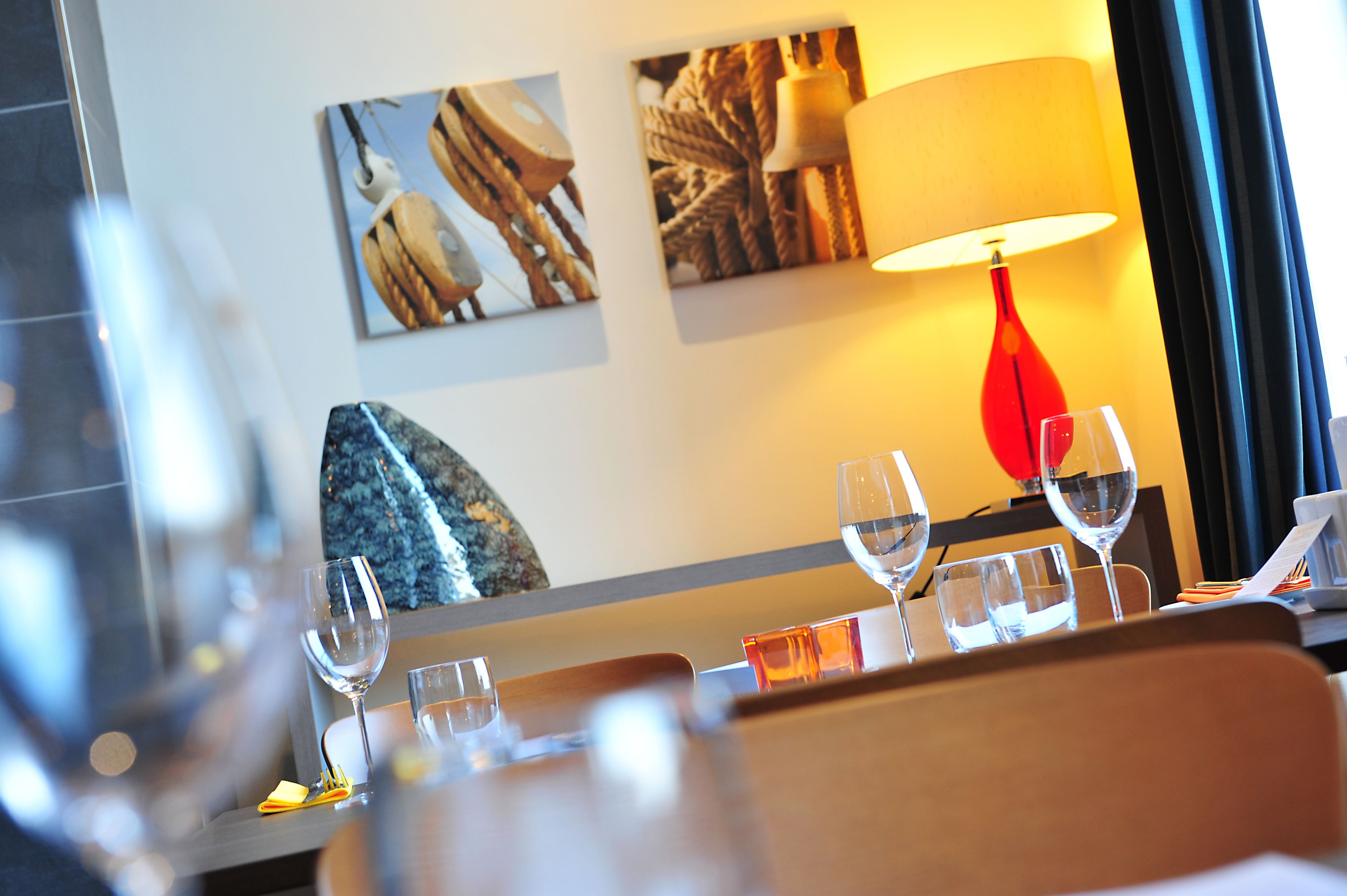 A hotel room with a dining table set for four, a red lamp, and artwork on the wall.