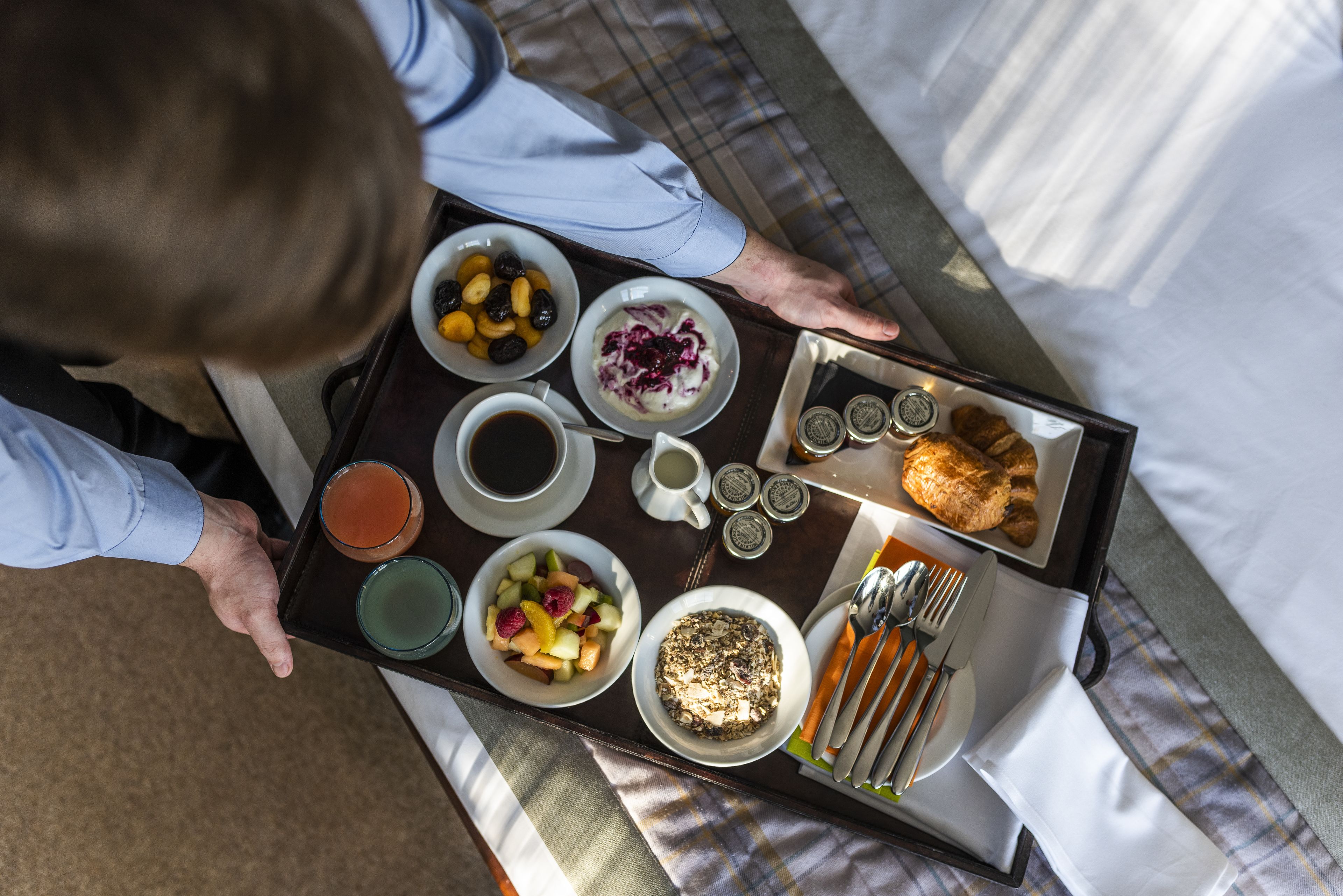 A tray with breakfast items including fruits, yogurt, coffee, and croissants.