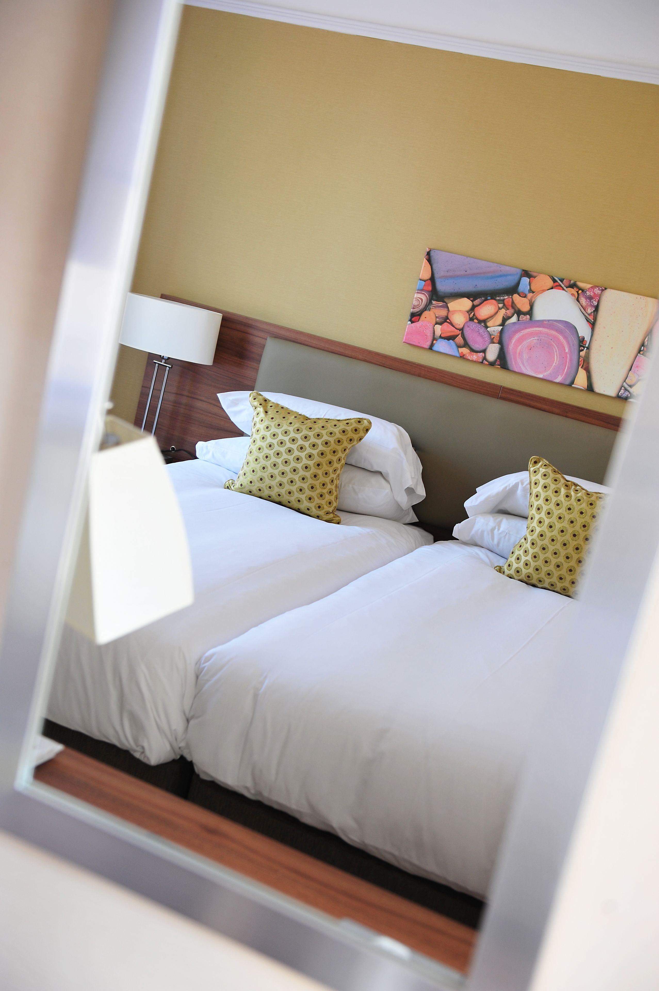 Ein Hotelzimmer mit zwei Betten, weißer Bettwäsche und einem farbenfrohen, abstrakten Gemälde an der Wand.