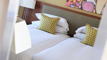 Ein Hotelzimmer mit zwei Betten, weißer Bettwäsche und einem farbenfrohen, abstrakten Gemälde an der Wand.