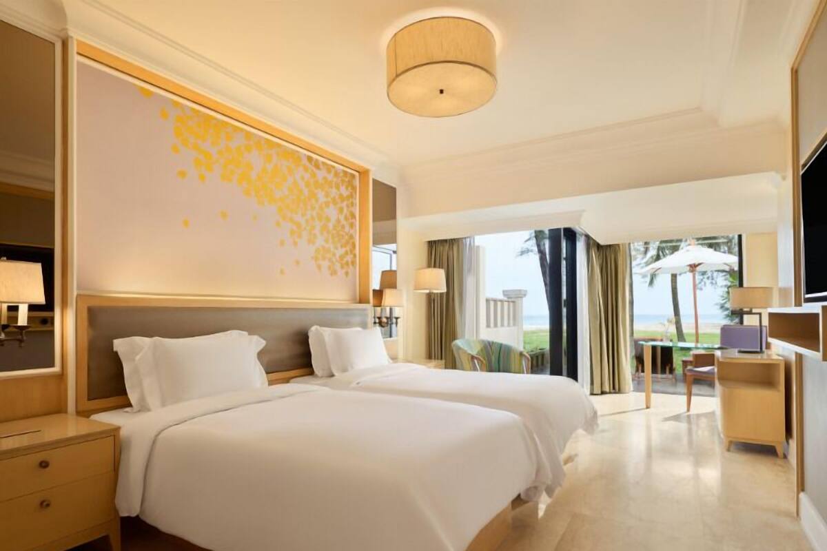 A hotel room with two beds, a large window with a view, a desk with a chair, and a TV.