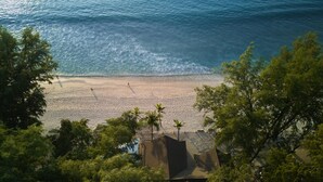 A beach with clear water, palm trees, and a building in the foreground. - Dusit Thani Laguna Phuket (Choeng Thale)