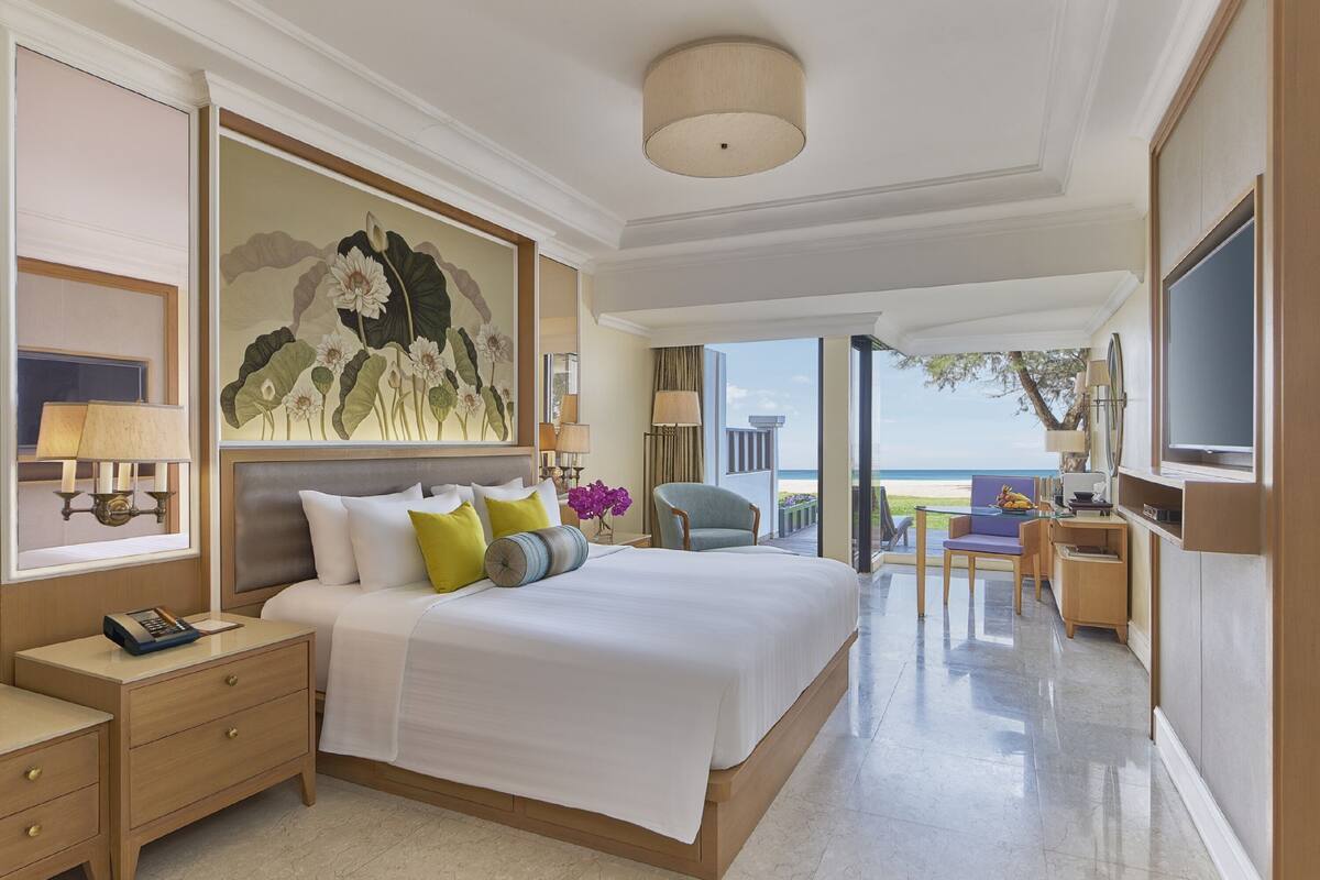 A spacious bedroom with a large bed, a desk, and a TV.