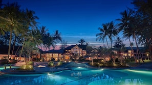 A resort with a swimming pool, palm trees, and a large building with multiple levels. - Dusit Thani Laguna Phuket (Choeng Thale)