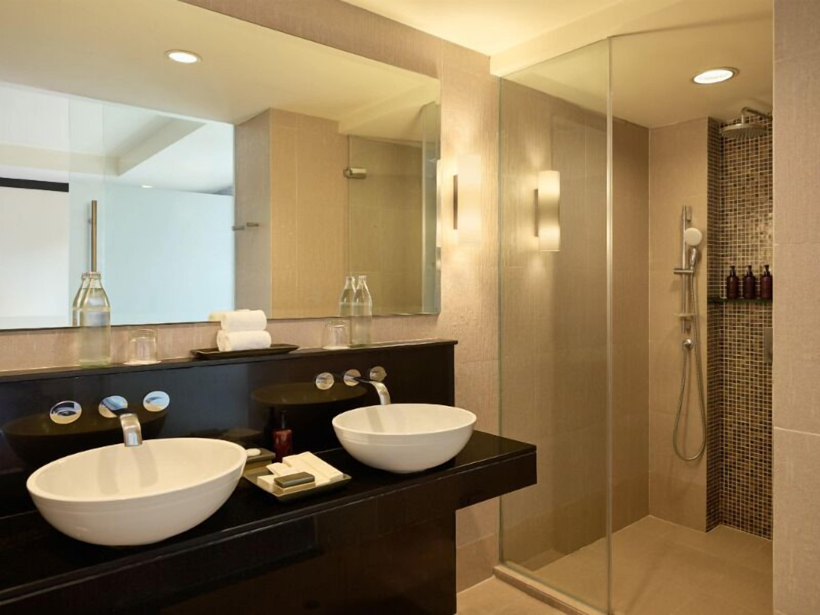 A modern bathroom with two large white sinks, a dark vanity, a large mirror, and a glass-enclosed shower area.
