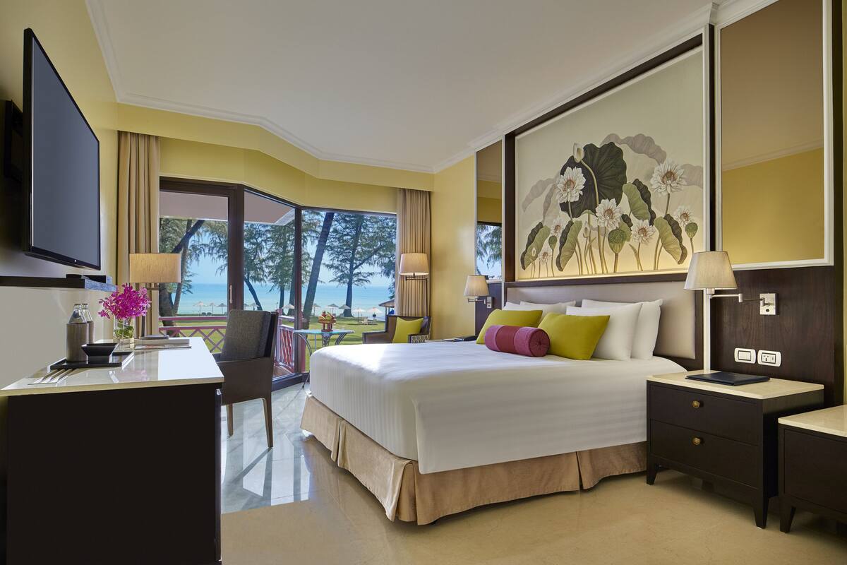 A hotel room with a large bed, a desk, a television, and a view of the ocean.