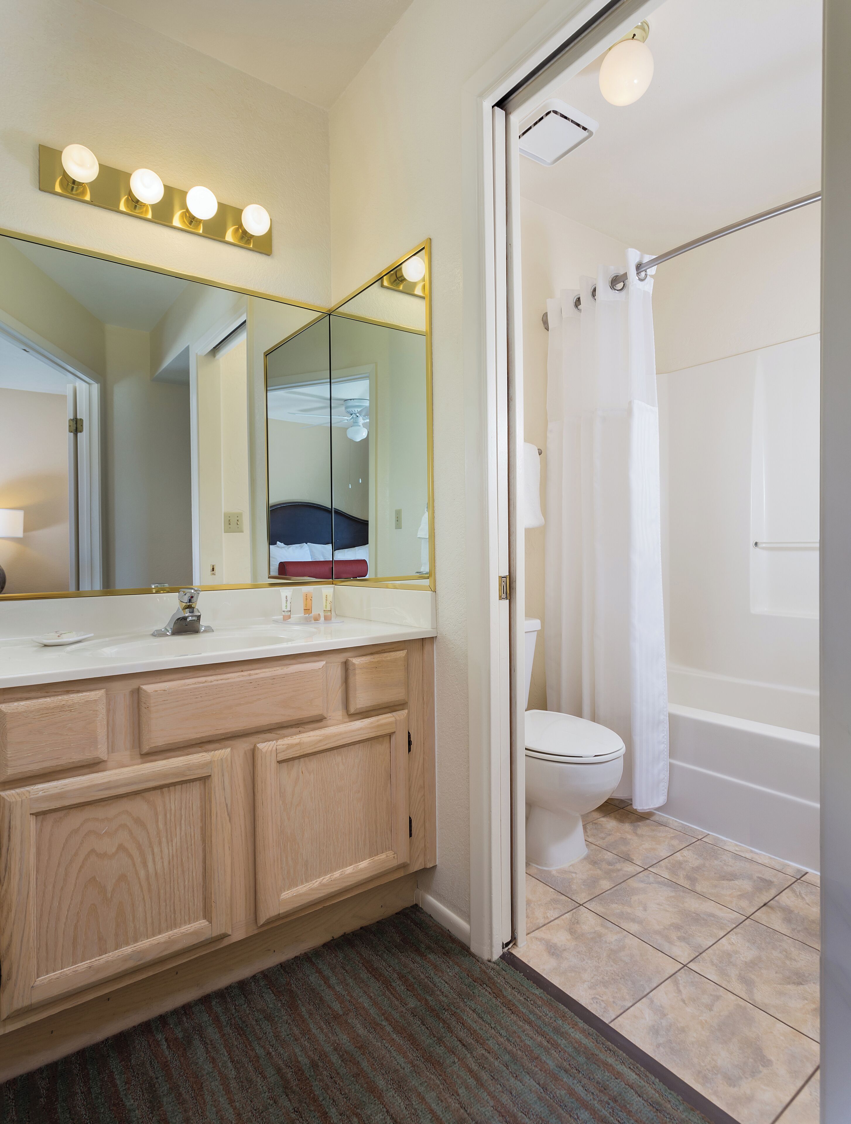 A bathroom with a wooden vanity, a large mirror, a toilet, and a bathtub.