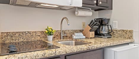 A kitchen with granite countertops, a stainless steel sink, a microwave, a coffee maker, and dark wooden cabinets.