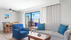 Ein modernes Wohnzimmer mit Essbereich, einer Couch, einem Couchtisch und Blick auf Palmen durch große Fenster.