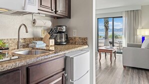 Eine moderne Küche mit Granit Arbeitsplatten, einem eingebauten Backofen und einer Kaffeemaschine. Es gibt einen Essbereich mit Tisch und Stühlen sowie einen Blick ins Freie.