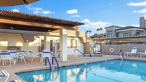 Ein Swimmingpool mit Liegestühlen und einem überdachten Bereich, umgeben von Gebäuden.