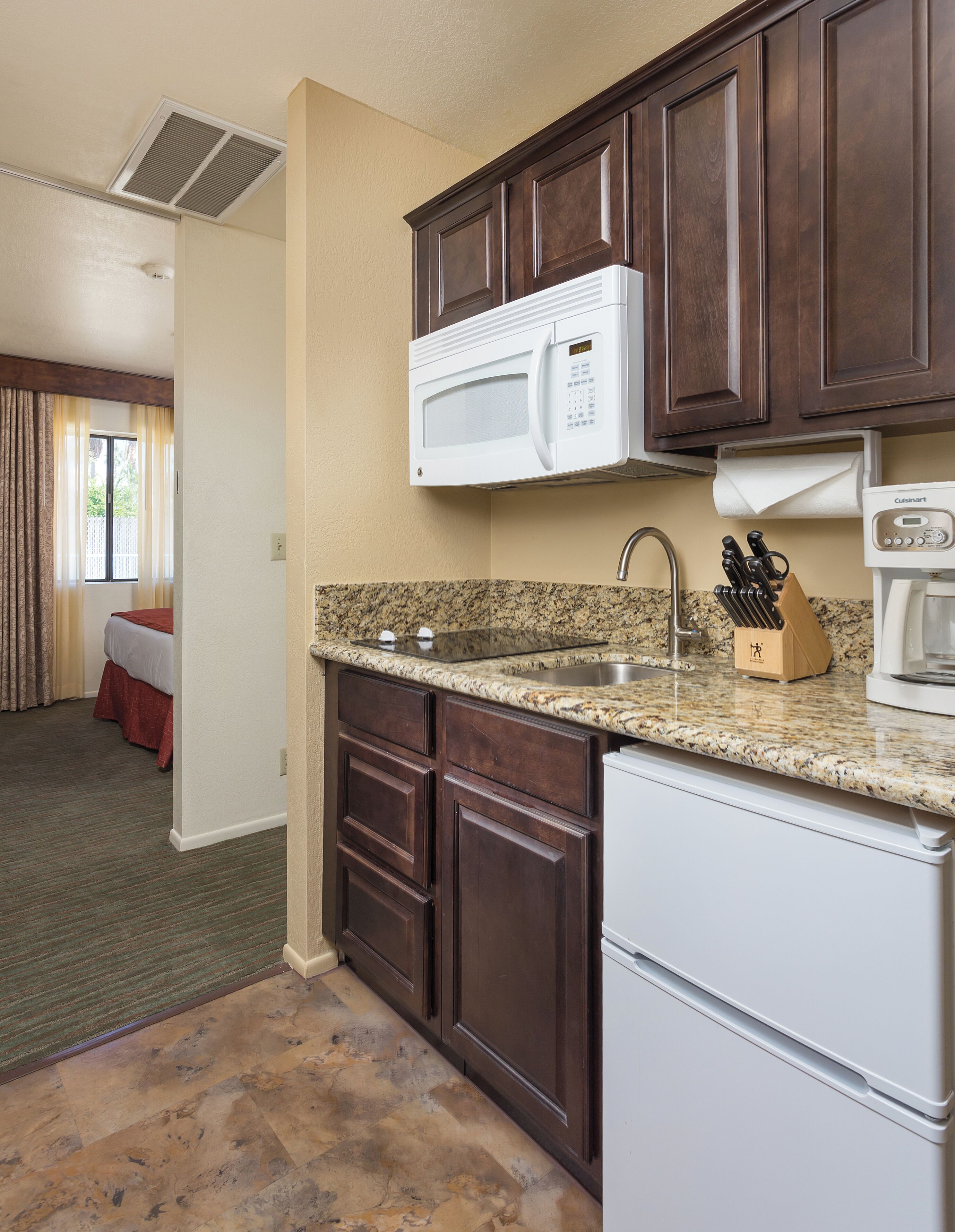 A compact kitchen with dark wooden cabinets, a granite countertop, a built-in microwave, a coffee maker, and a sink.