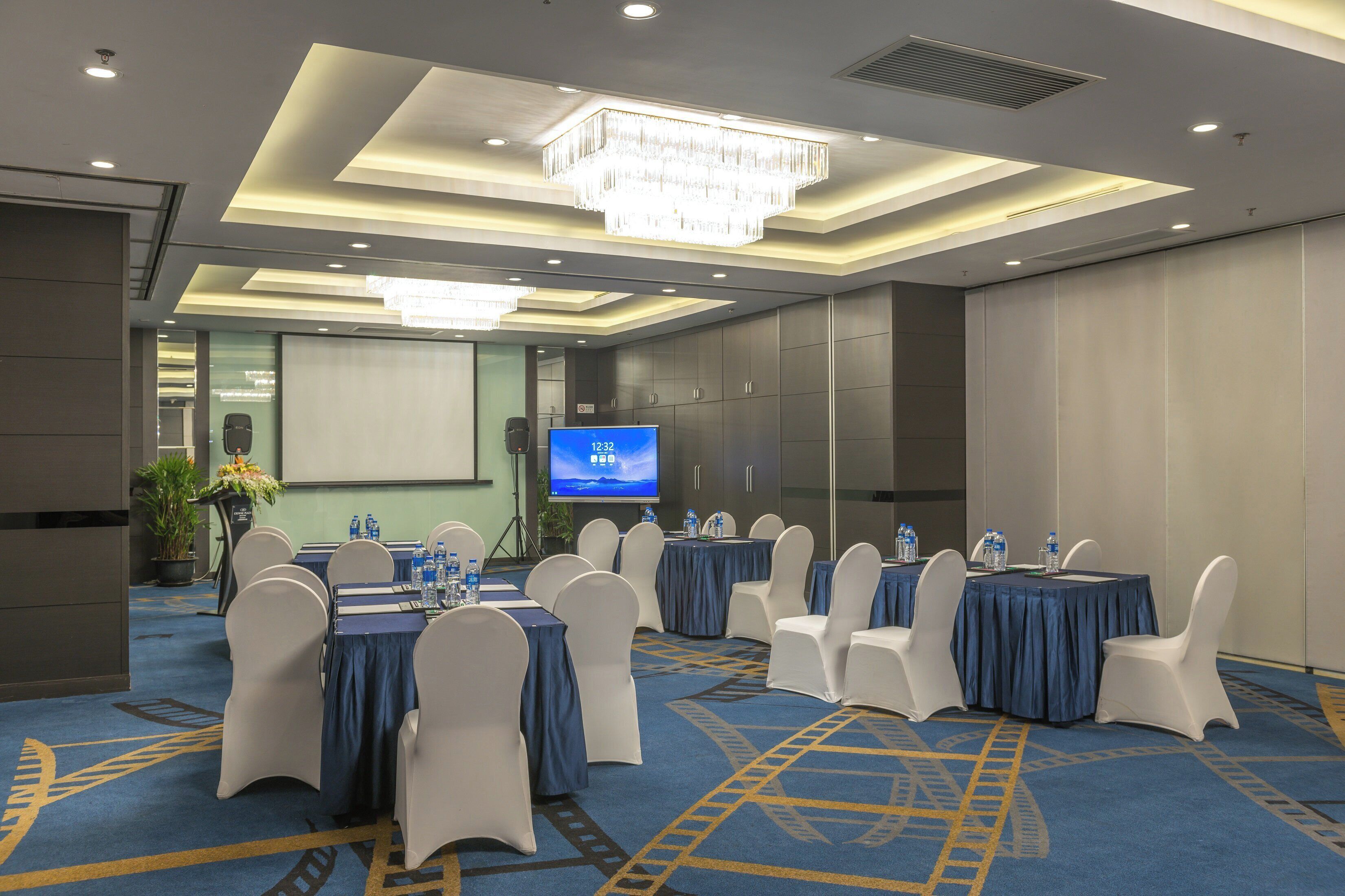 A conference room with tables, chairs, a projector screen, and a chandelier.